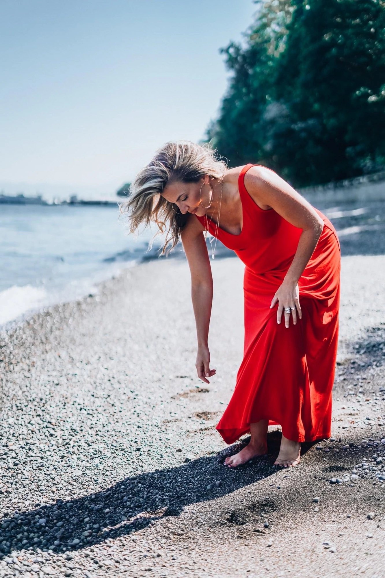 J Muenz smiling in a red dress by the water