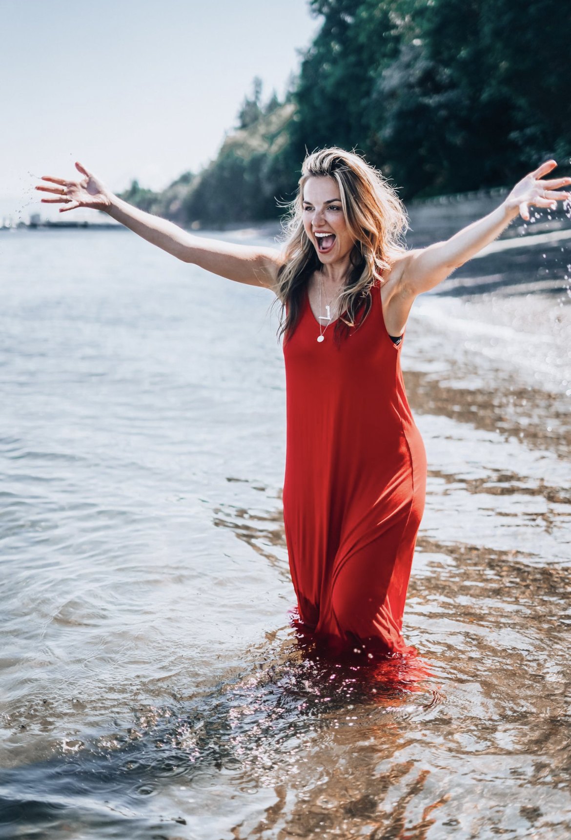 J Muenz in a red dress, arms open in the water